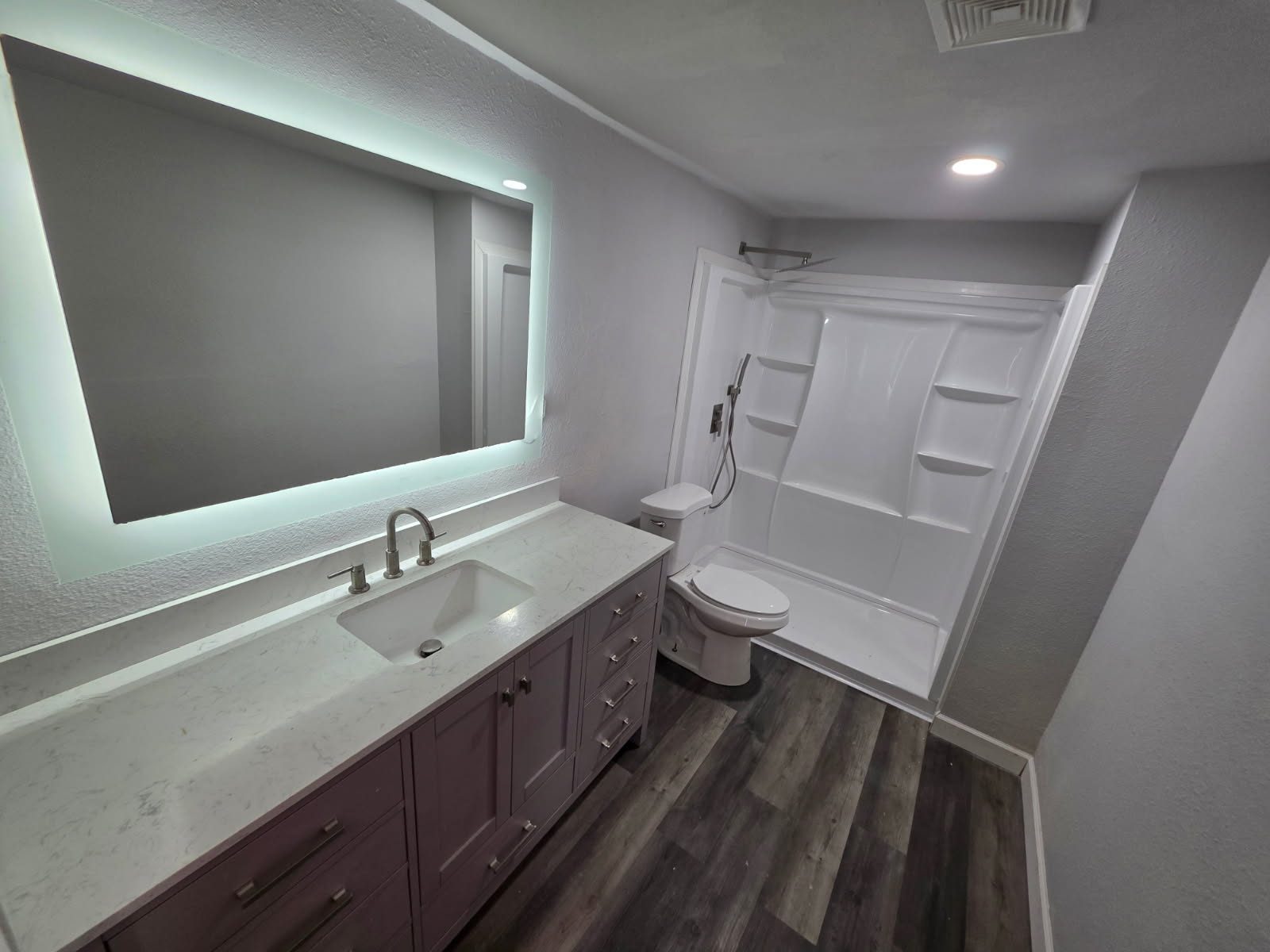 Remodeled bathroom with a backlit LED mirror, quartz vanity and new tub-shower surround