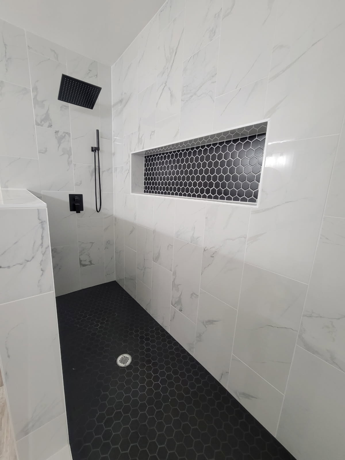 Custom walk-in shower with marble-look tile, black hex floor and matte black fixtures